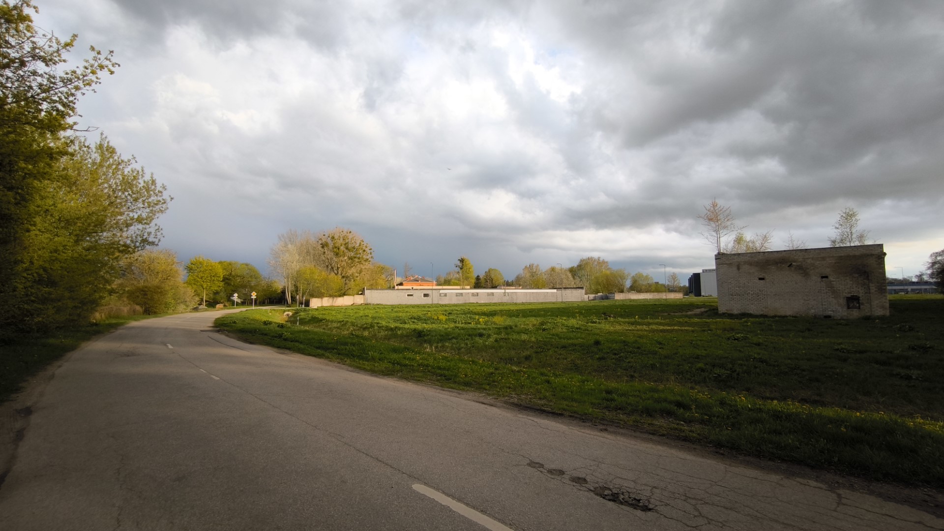 A photo of a landscape. Along the left side of the photo there is a road curving to the right and a building can be seen on the very right.